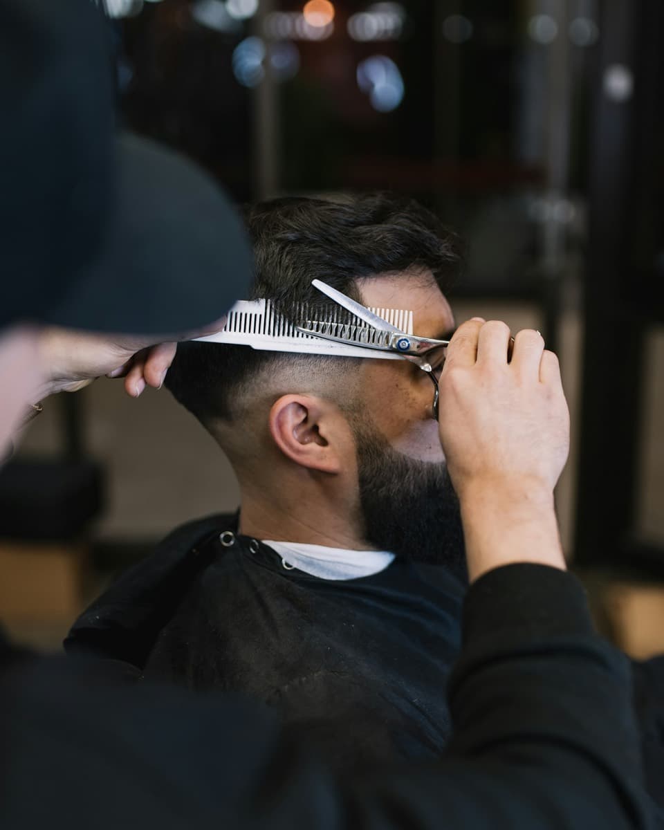 Barber cutting hair with scissors over comb